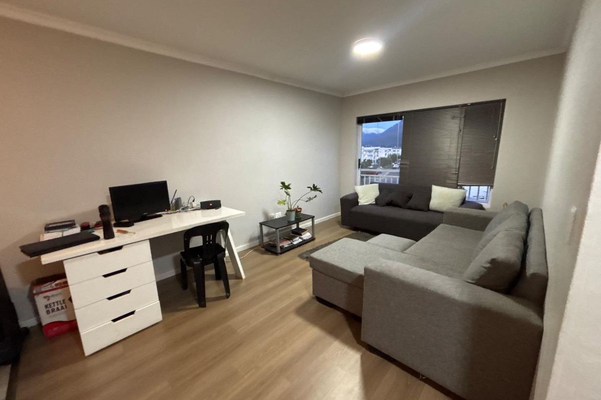 A well-maintained living room featuring durable laminate flooring, neutral wall finishes, and venetian blinds, offering a functional and comfortable space.