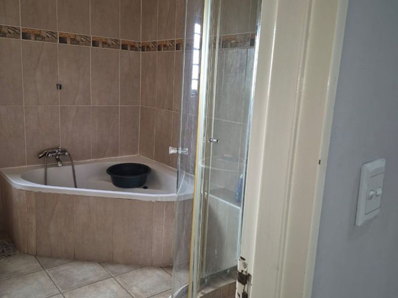 A functional bathroom featuring a corner bathtub and a separate curved glass shower enclosure with neutral ceramic tiling throughout.