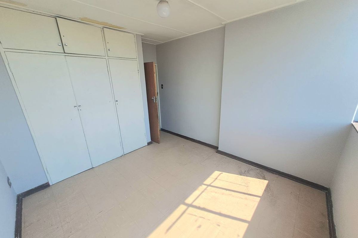 An empty bedroom featuring built-in cupboards and tiled flooring, offering a blank canvas for renovation and interior design updates.