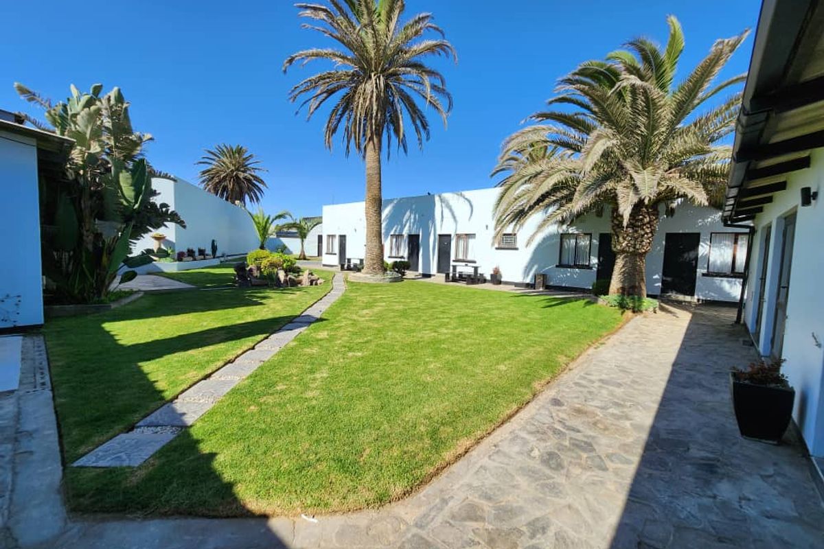A well-maintained courtyard garden area featuring manicured lawns, stone pathways, and mature palm trees, surrounded by hotel room entrances.