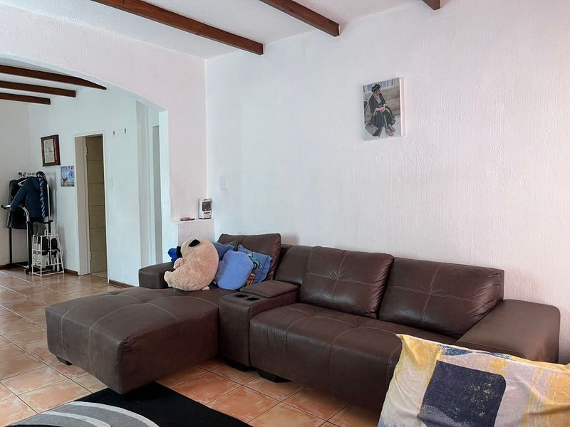 A living room featuring exposed timber ceiling beams, ceramic floor tiles, and an arched doorway leading to an adjacent space.