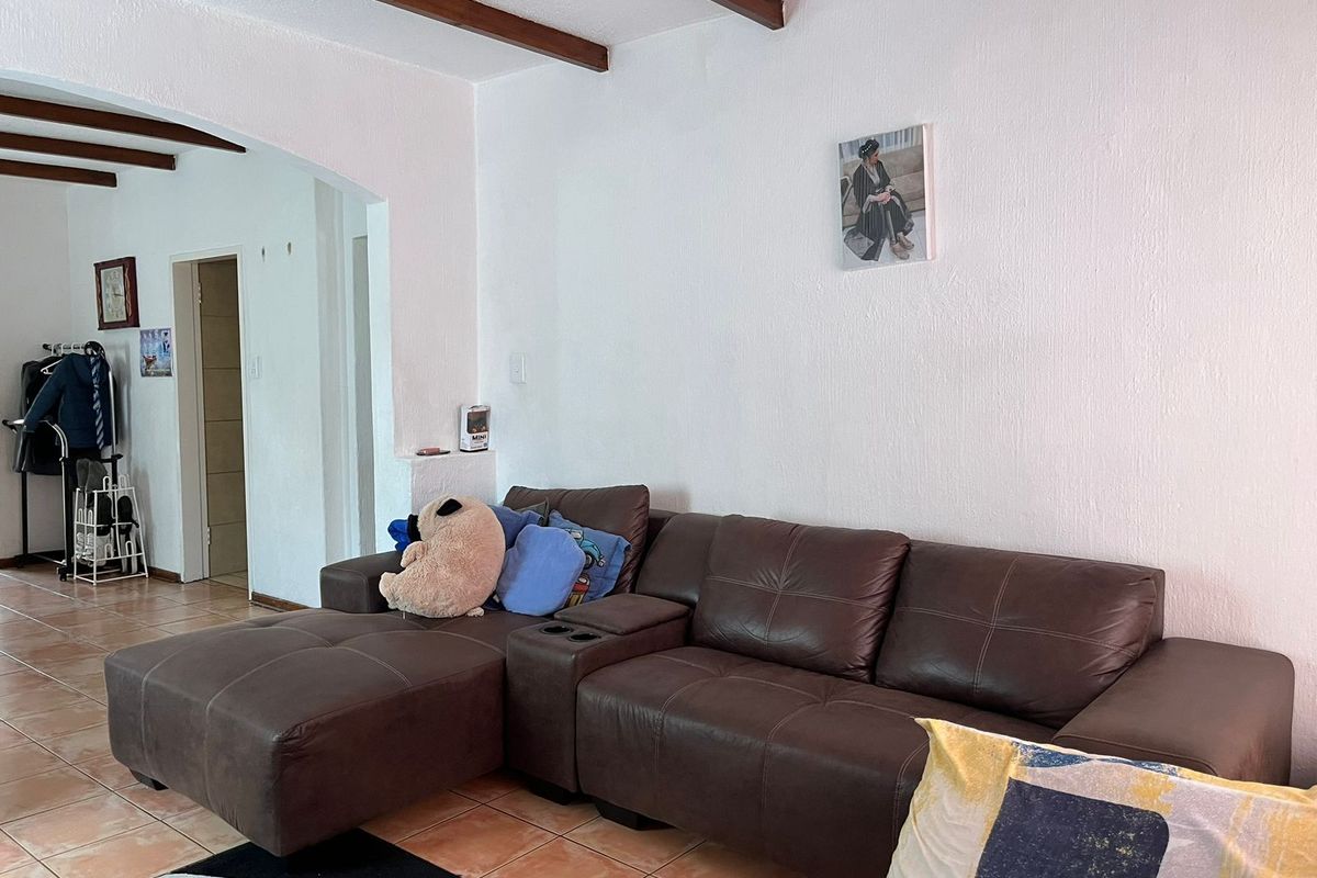A living room featuring exposed timber ceiling beams, ceramic floor tiles, and an arched doorway leading to an adjacent space.