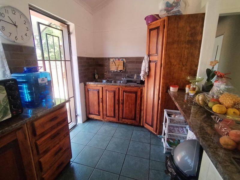 A functional scullery area featuring wooden cabinetry, granite countertops, a double sink, and tiled finishes with direct access to the exterior.
