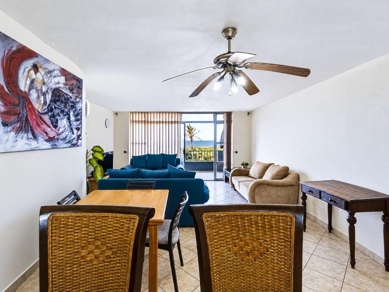 Spacious open-plan living and dining area featuring tiled flooring, a ceiling fan, and direct access to a balcony with ocean views.