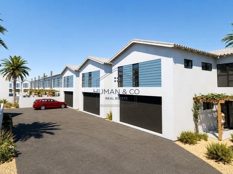 Modern townhouse complex featuring clean white facades, dark sectional garage doors, and paved driveway access with integrated timber pergola elements.