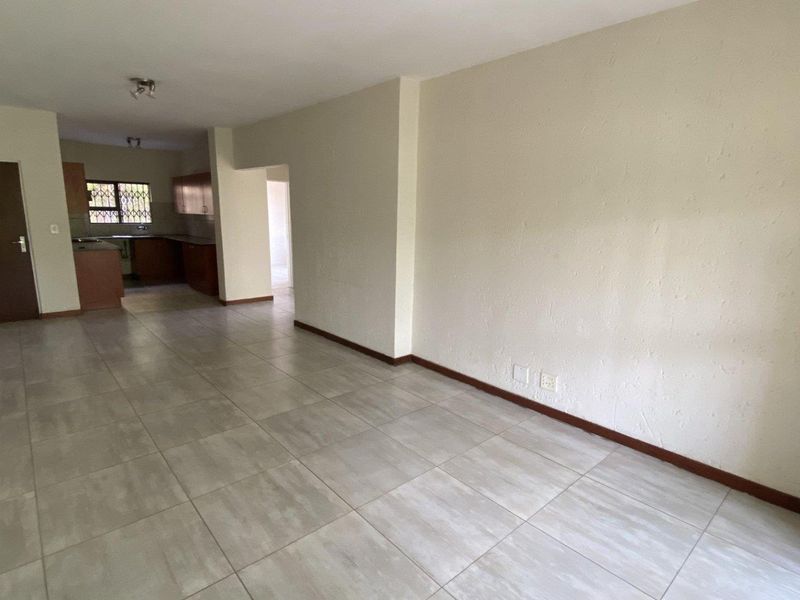 An empty open-plan living and kitchen area featuring neutral tiled flooring and wooden cabinetry, offering a blank canvas for interior design.