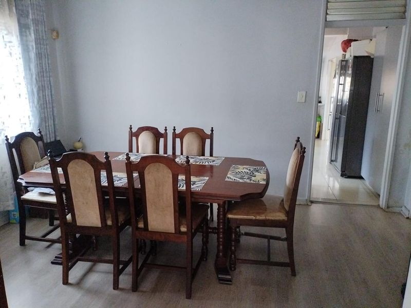 A functional dining room featuring laminate flooring and a neutral wall finish, with an open doorway leading to the kitchen area.