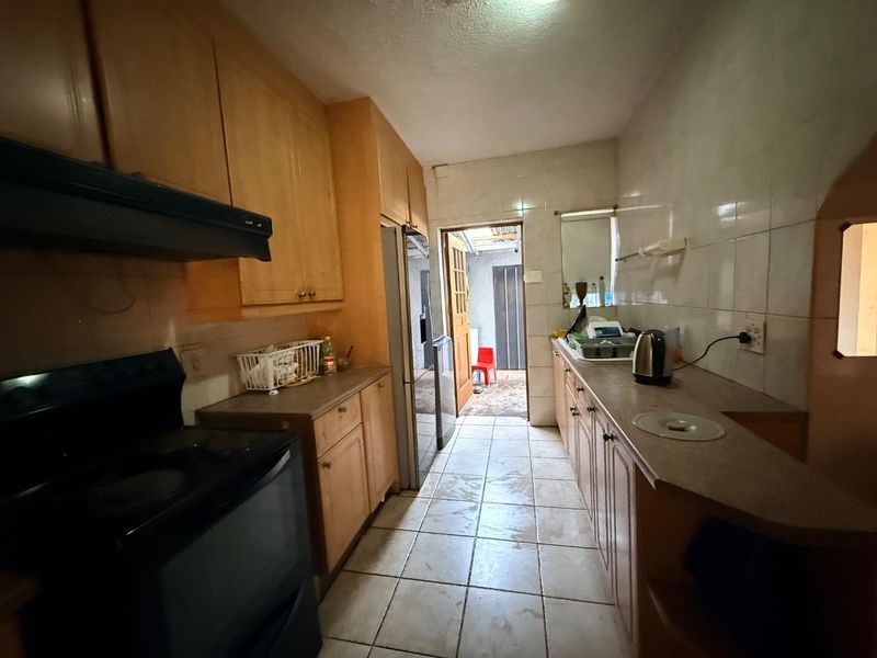 A functional galley-style kitchen featuring wooden cabinetry, tiled splashbacks, and tiled flooring, offering a practical layout with direct access to the rear exterior.