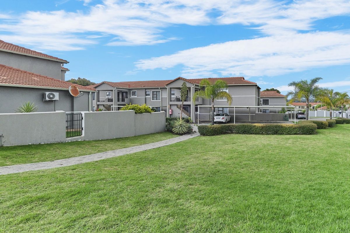 View of the townhouse complex exterior featuring landscaped lawns, paved walkways, and covered carport parking areas.
