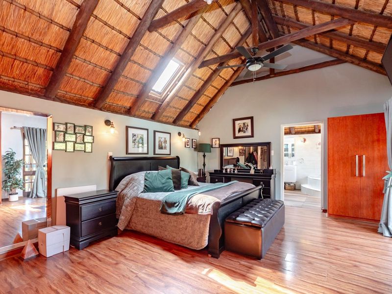 Spacious bedroom featuring a high vaulted thatch ceiling with exposed timber trusses, a skylight, ceiling fan, and direct access to an en-suite bathroom.