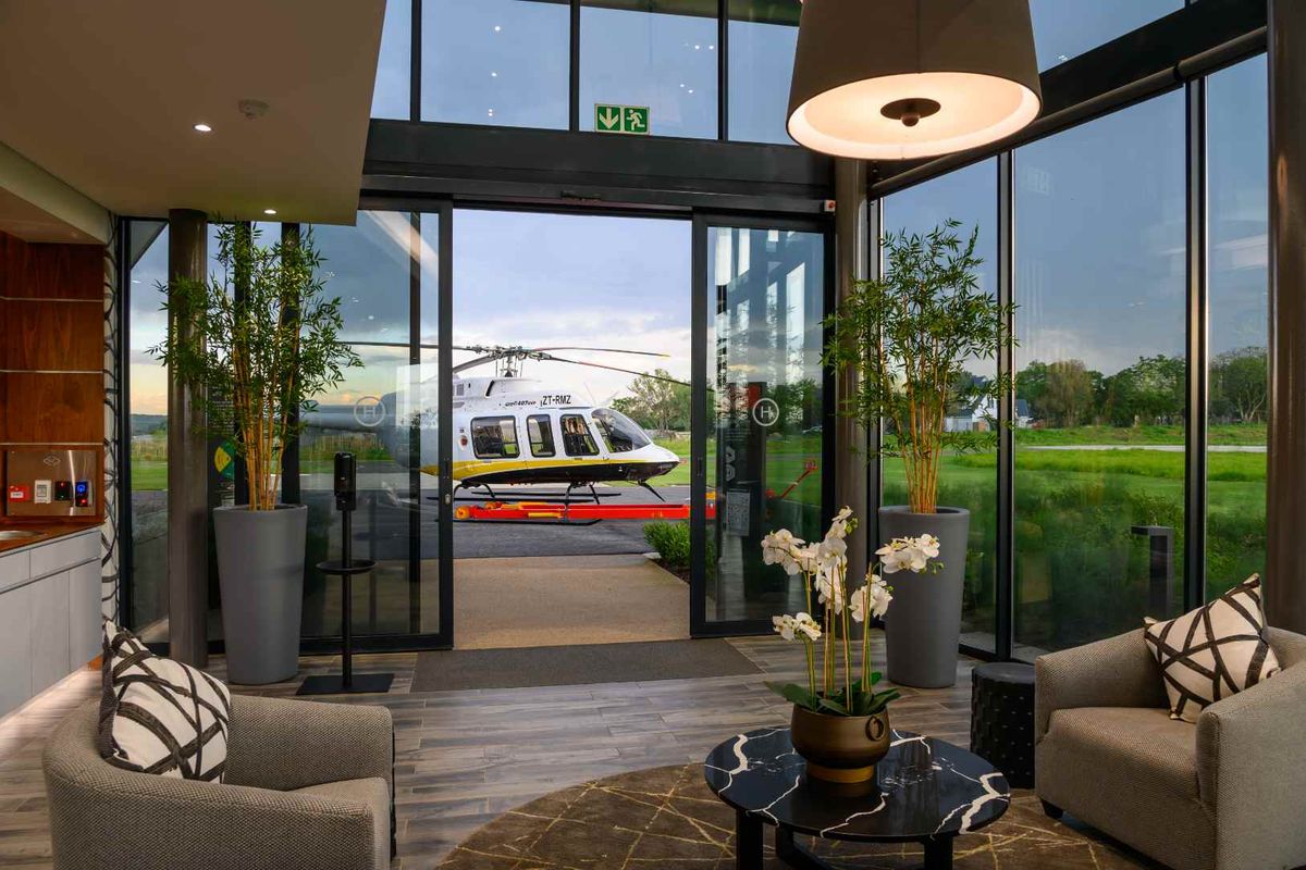 Modern lounge area featuring floor-to-ceiling glass walls with direct views of an outdoor helipad and landscaped grounds.