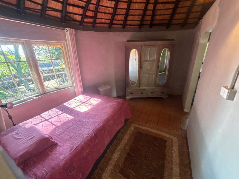 A bedroom featuring a traditional thatched roof, terracotta floor tiles, and diamond pane windows, offering a rustic cottage aesthetic.