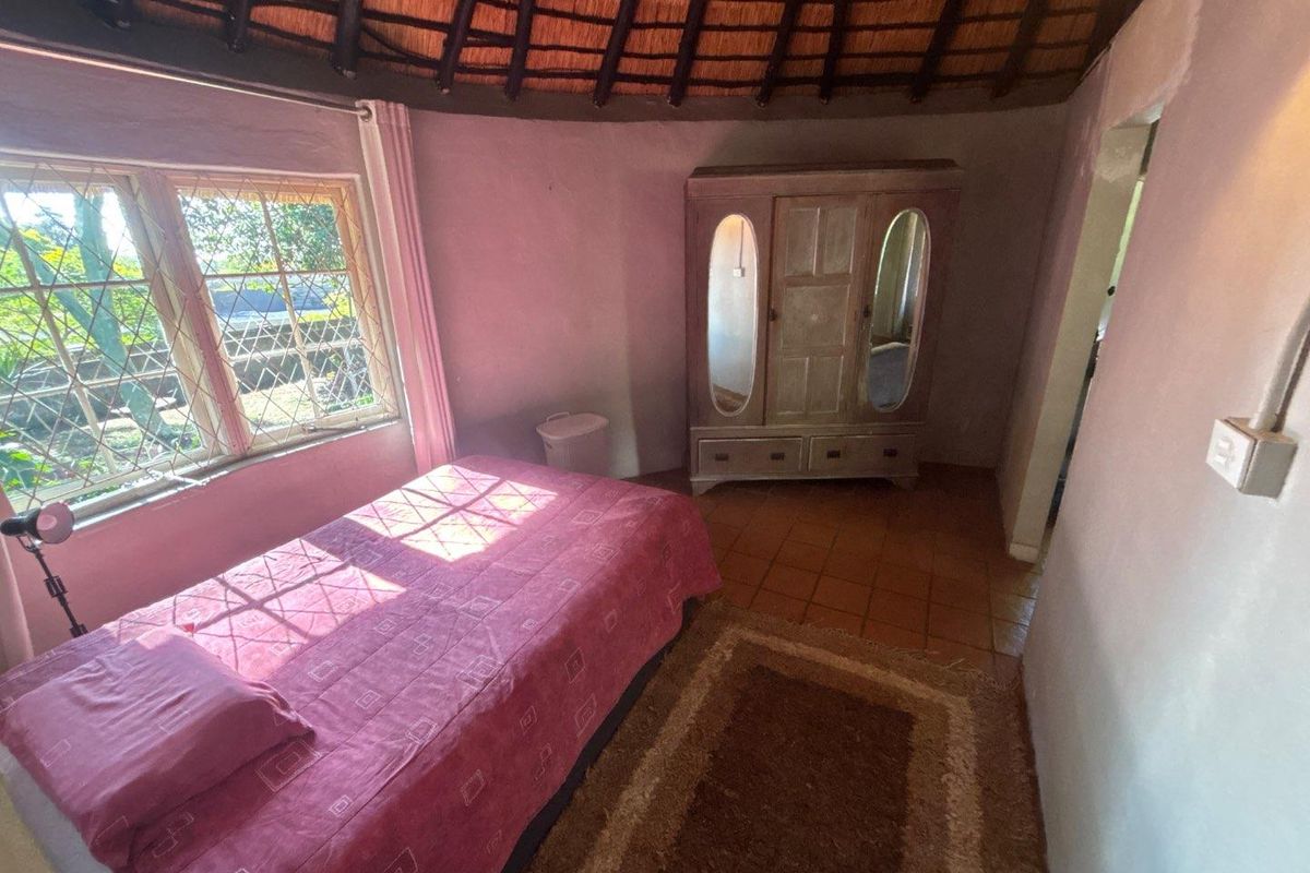A bedroom featuring a traditional thatched roof, terracotta floor tiles, and diamond pane windows, offering a rustic cottage aesthetic.
