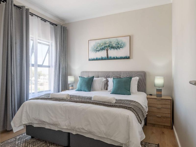 A well-maintained bedroom featuring neutral wall tones, laminate flooring, and a large window allowing for natural light.