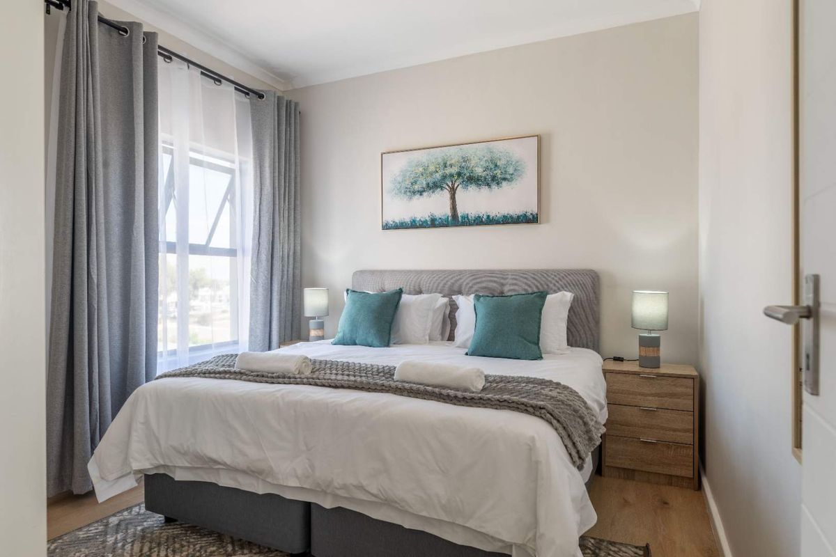 A well-maintained bedroom featuring neutral wall tones, laminate flooring, and a large window allowing for natural light.