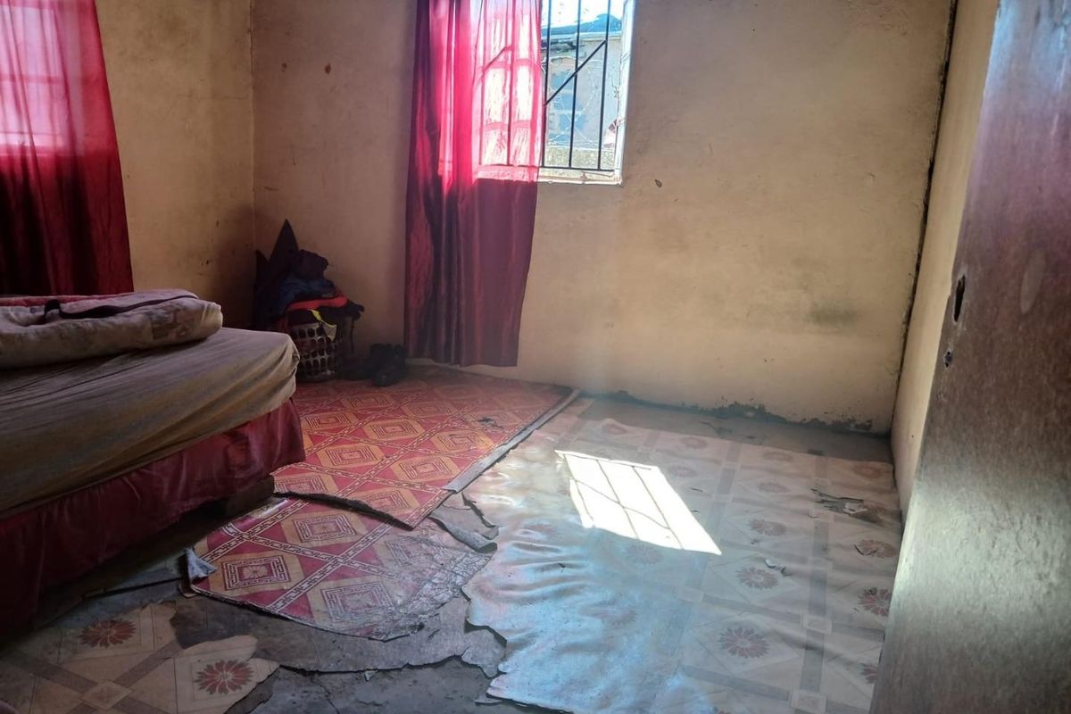 A bedroom interior showing significant wear, including damaged flooring and stained wall surfaces, requiring renovation and repair.