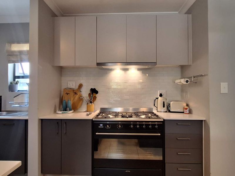 Modern kitchen featuring sleek grey cabinetry, quartz countertops, a subway tile backsplash, and high-quality built-in gas cooking appliances.