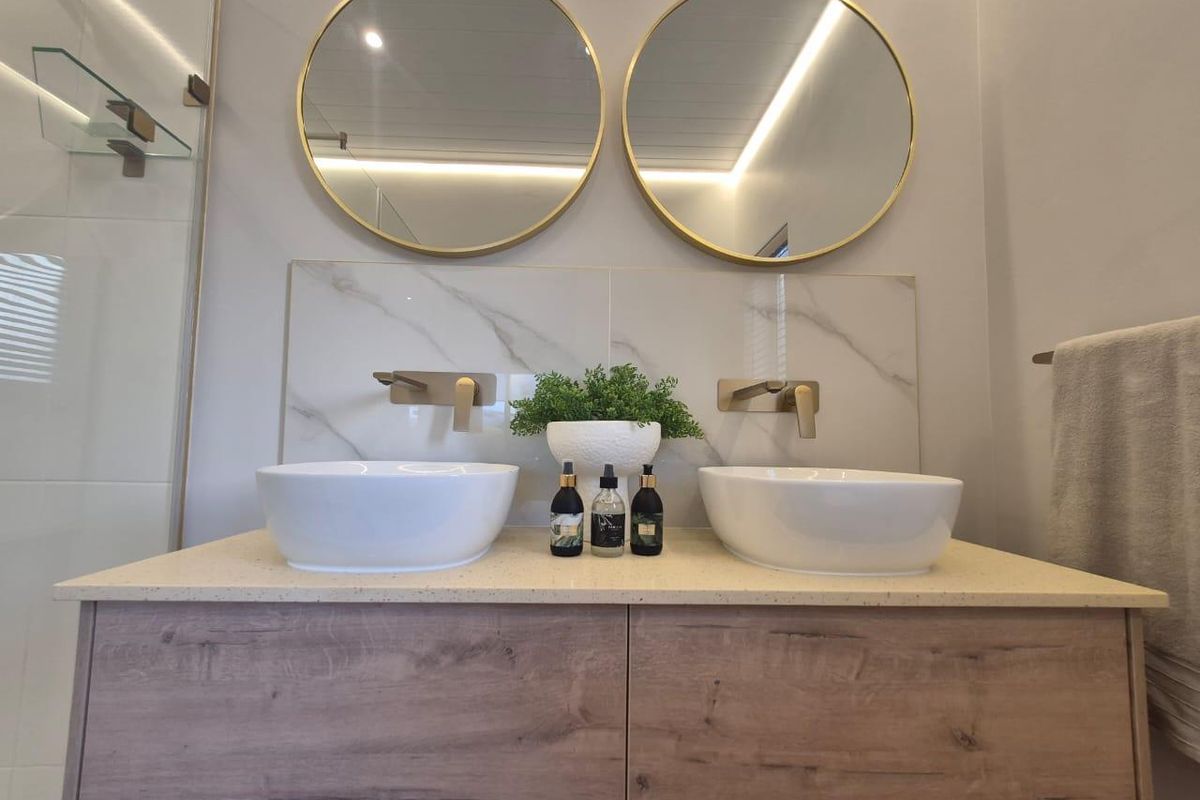 Modern bathroom featuring a double vanity with vessel sinks, wall-mounted gold-tone faucets, marble-look splashback, and round mirrors.