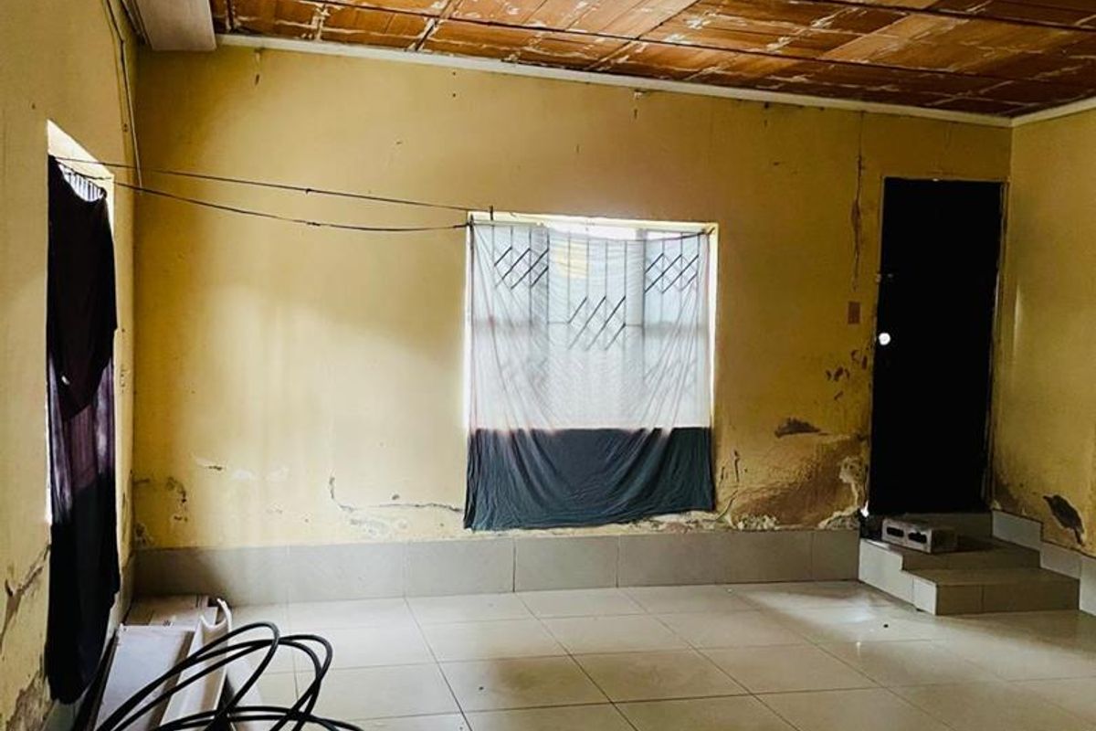 An empty living room featuring tiled flooring and a timber panel ceiling, currently requiring significant wall and ceiling repairs and cosmetic updates.