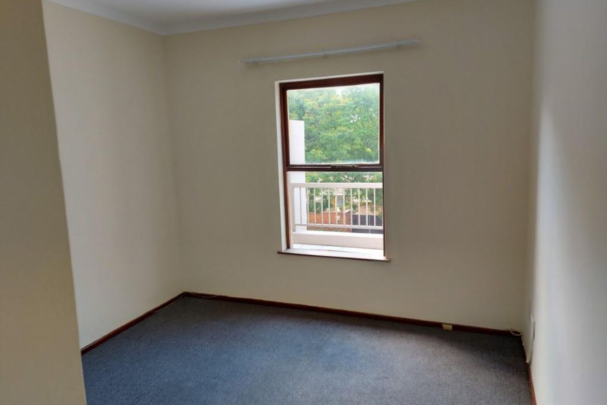 A clean, empty bedroom featuring neutral walls, carpeted flooring, and a window with a view of the exterior balcony.