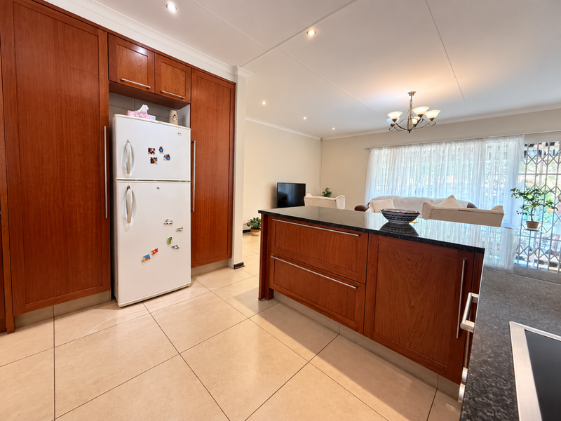 Open-plan kitchen and living area featuring warm wood cabinetry, granite countertops, tiled floors, and direct access to a patio through sliding glass doors.