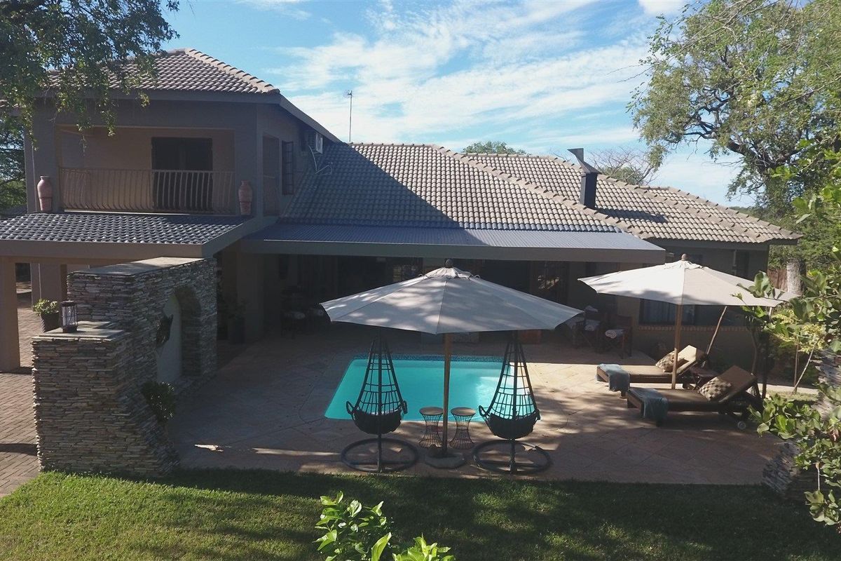 Rear view of the property featuring a paved patio area, a swimming pool, and a covered outdoor entertainment space with a balcony above.