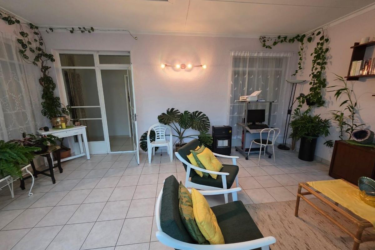 A bright living room featuring tiled flooring, a glass panel door, and wall-mounted lighting, offering a versatile space for relaxation.