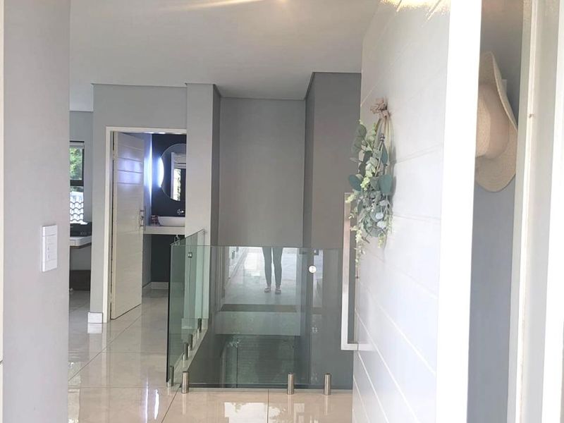 A bright, modern hallway featuring polished tiled flooring and a contemporary glass balustrade overlooking the lower level.