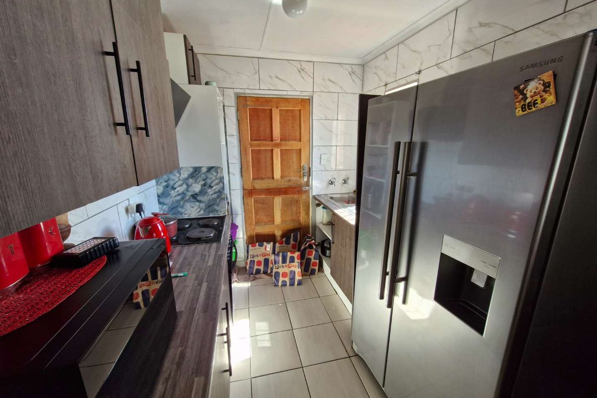 A functional kitchen featuring dark wood-look cabinetry, marble-effect wall tiles, tiled flooring, and a stainless steel double-door refrigerator.