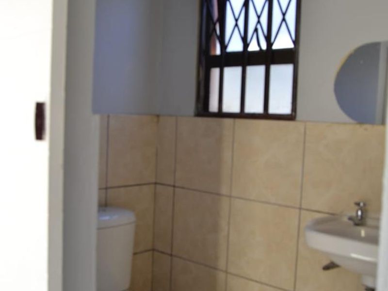 A functional bathroom featuring a toilet, wall-mounted basin, and neutral tiled finishes with a secure window.