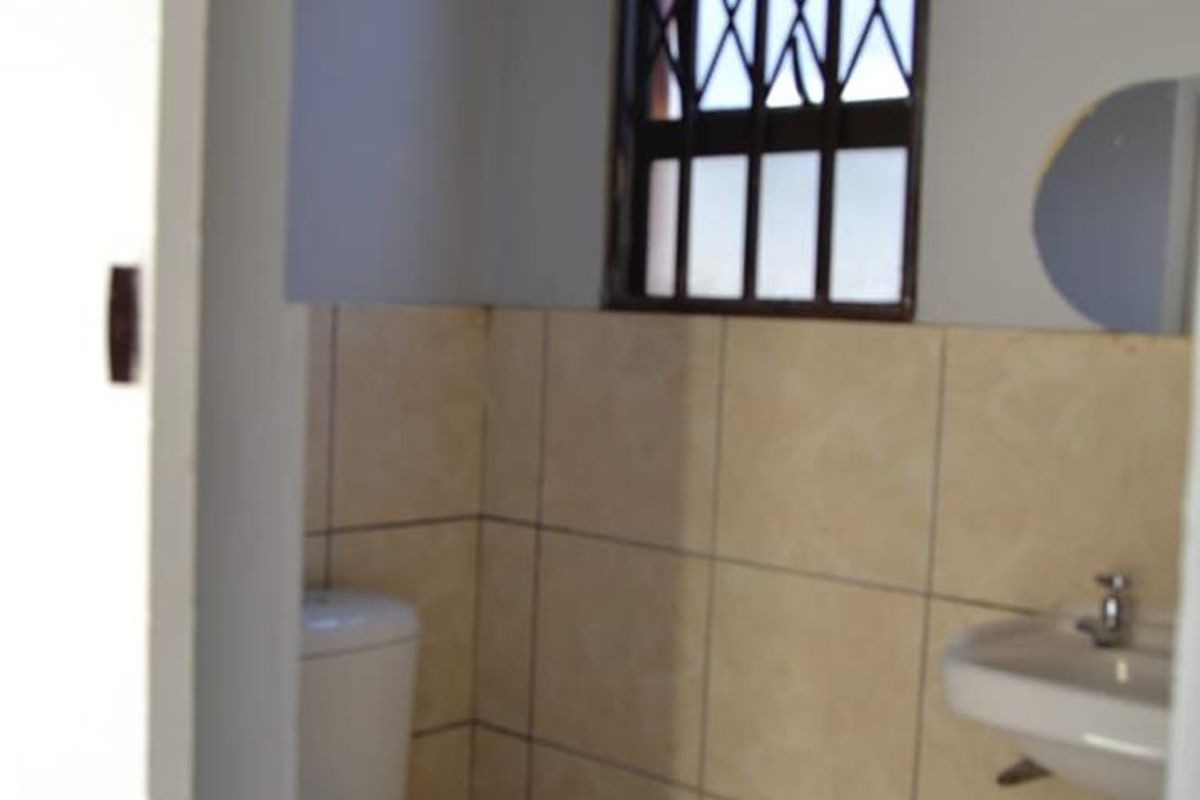 A functional bathroom featuring a toilet, wall-mounted basin, and neutral tiled finishes with a secure window.