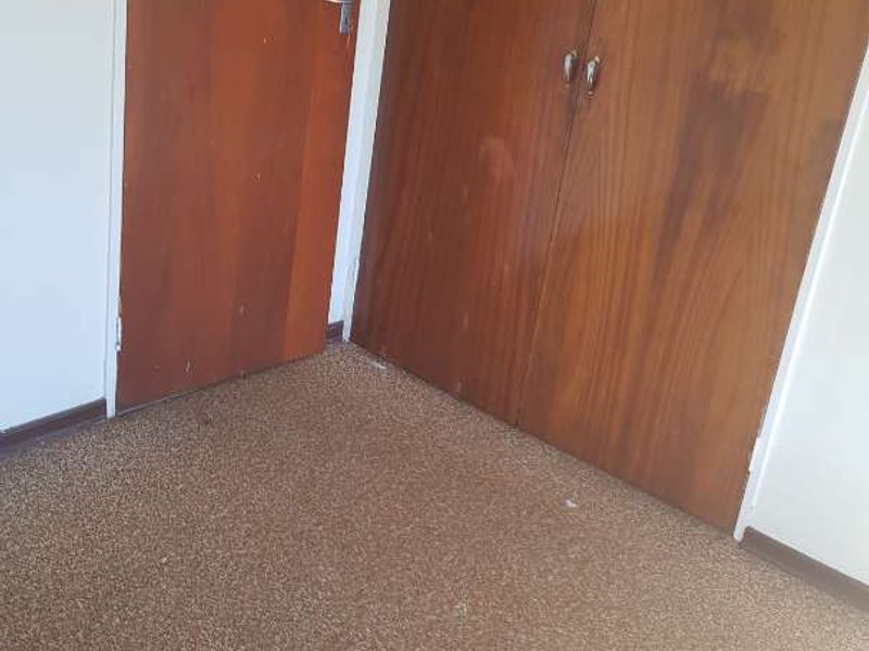 An empty bedroom featuring built-in wooden cupboards and carpeted flooring, offering a blank canvas for renovation or restyling.