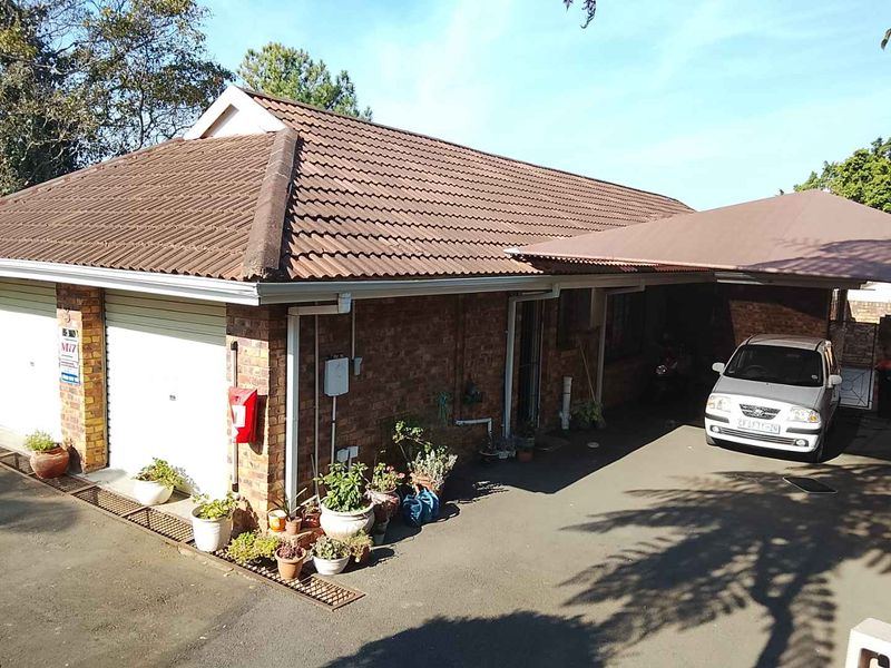 Front exterior view of a brick townhouse featuring a tiled roof, double garage, and an attached carport over the driveway.