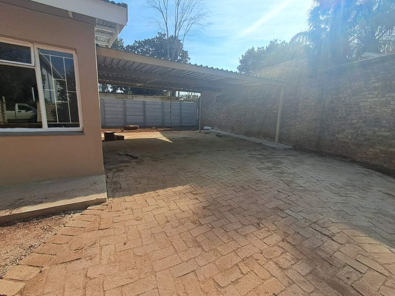 A spacious outdoor area featuring a covered carport, paved driveway, and secure perimeter walling, suitable for vehicle parking or outdoor storage.