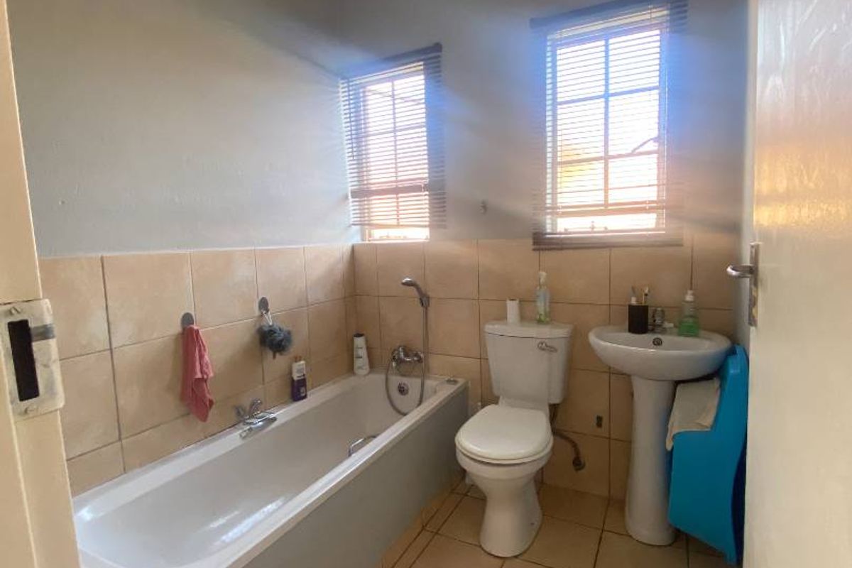 A functional bathroom featuring a standard bathtub, pedestal basin, and toilet with tiled flooring and partial wall tiling.
