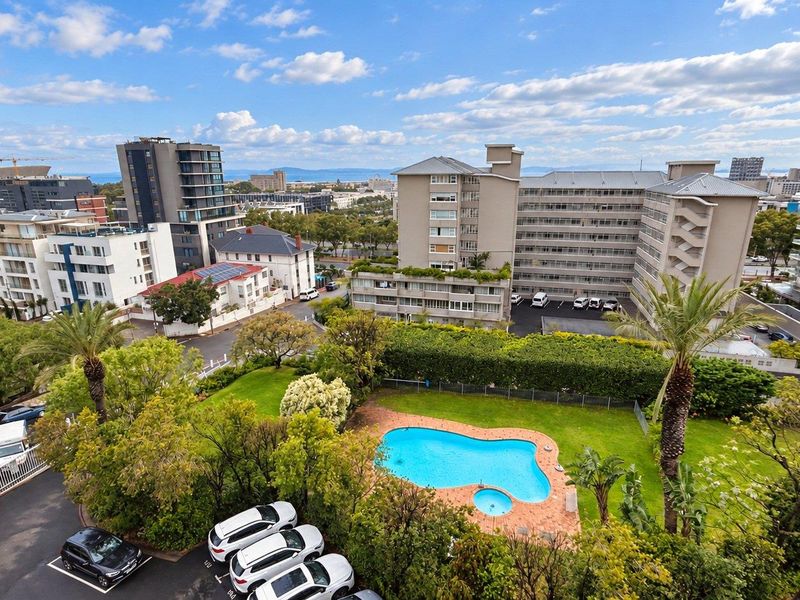 An elevated aerial view of the apartment complex grounds, featuring a swimming pool, manicured lawn, and surrounding residential buildings.