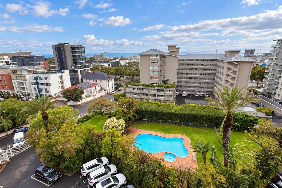 An elevated aerial view of the apartment complex grounds, featuring a swimming pool, manicured lawn, and surrounding residential buildings.