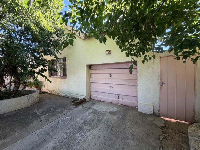 Exterior view of a single garage featuring a concrete driveway, steel window frame, and a side access door, showing signs of wear and weathering.