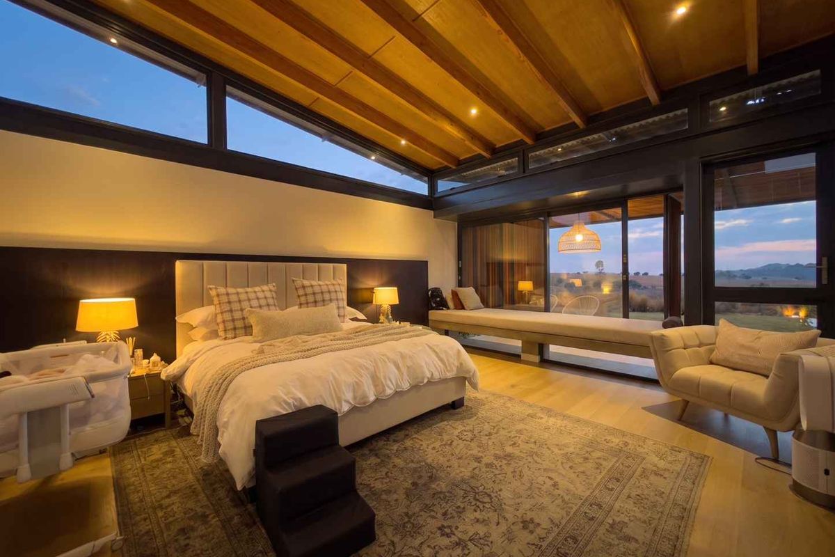 Spacious modern bedroom featuring exposed timber beam ceilings, clerestory windows, and large sliding glass doors that open to scenic views with a built-in window bench.