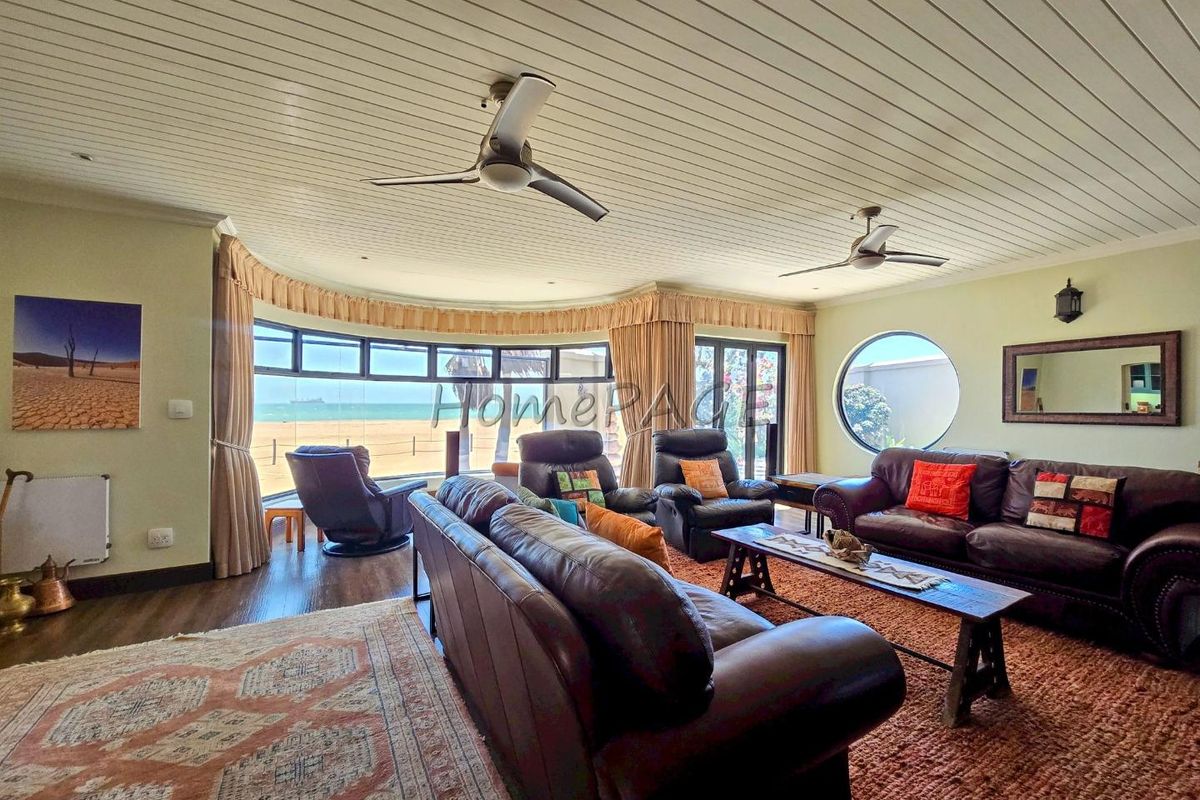 Spacious living room featuring a unique curved window with ocean views, circular accent window, tongue and groove ceiling, and dual ceiling fans.