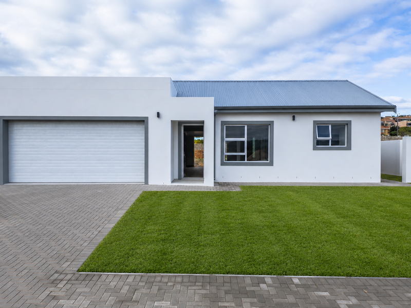 Modern single-story home featuring a clean white facade, integrated garage, metal roof, and a well-maintained front lawn with paved driveway.