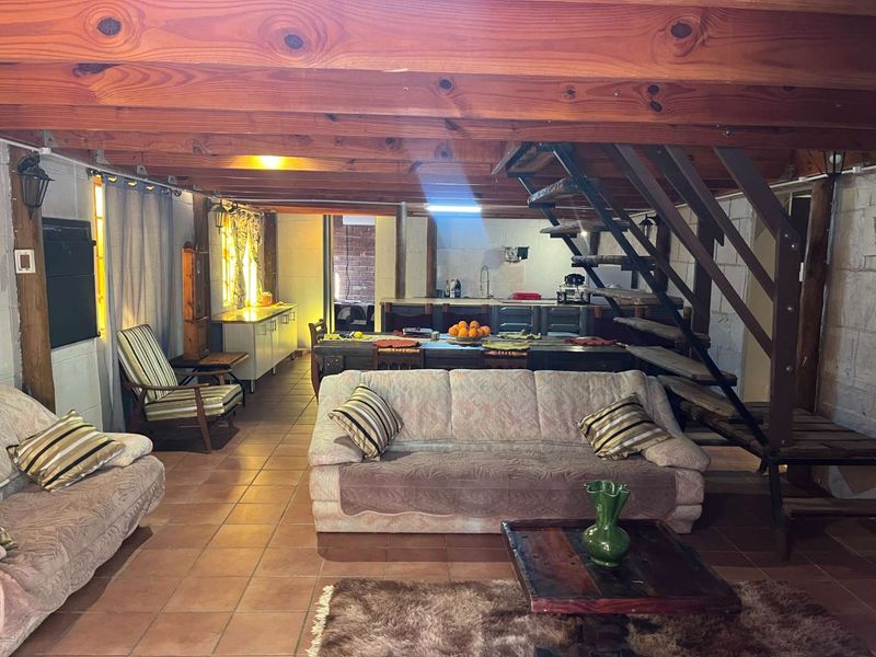 Open-plan living and kitchen area featuring exposed timber ceiling beams, tiled flooring, and a staircase, offering a rustic and functional layout.