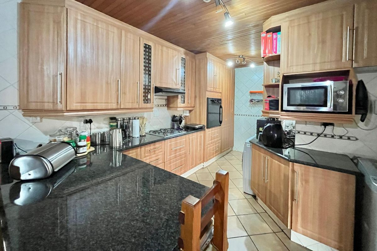 A functional kitchen featuring light wood cabinetry, dark granite countertops, a built-in oven, gas hob, and a timber-paneled ceiling.