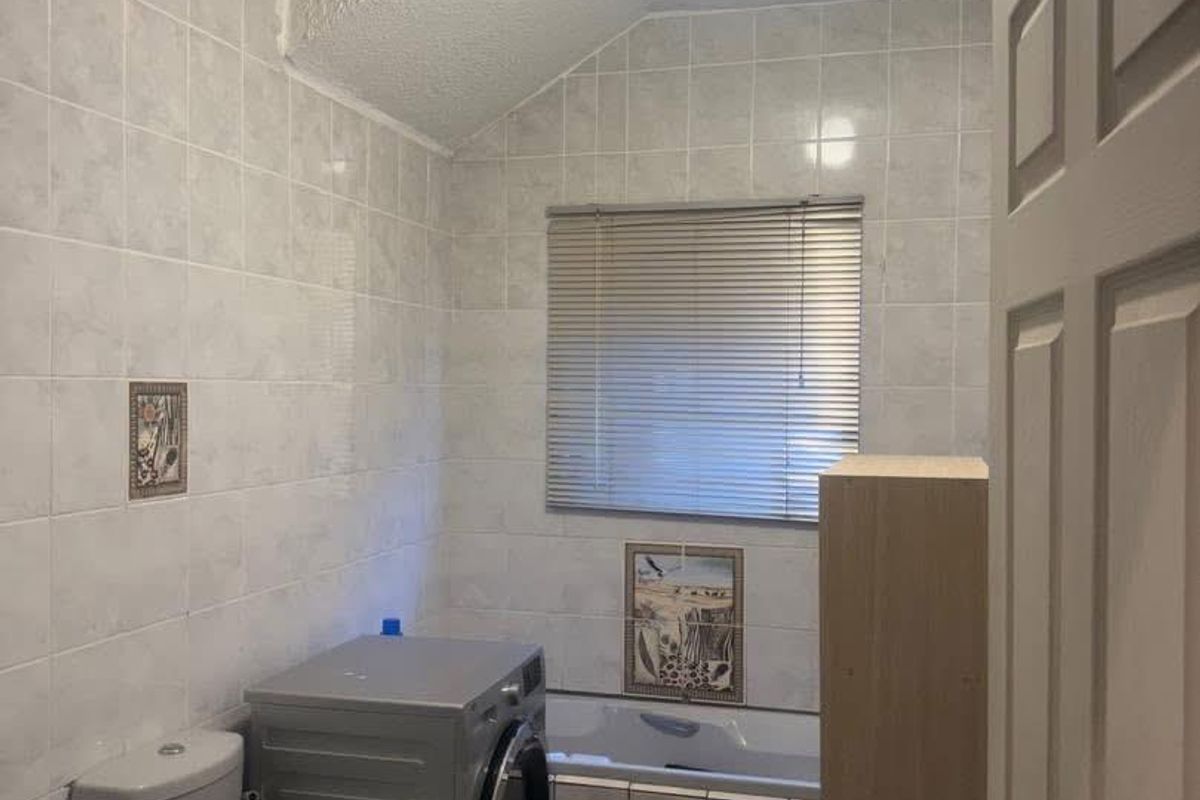A functional bathroom featuring a bathtub, toilet, and integrated laundry space with tiled walls and flooring.