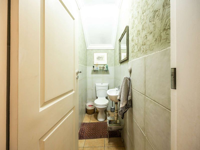 A compact guest bathroom featuring a pedestal sink, toilet, and neutral tiled finishes with decorative wallpaper.