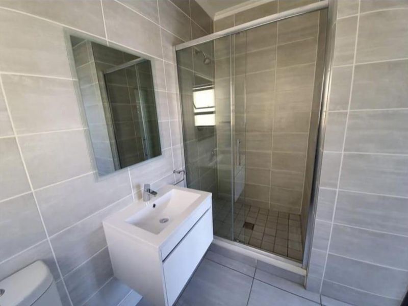 Modern bathroom featuring a wall-mounted vanity, a glass-enclosed shower, and neutral ceramic tiling throughout.