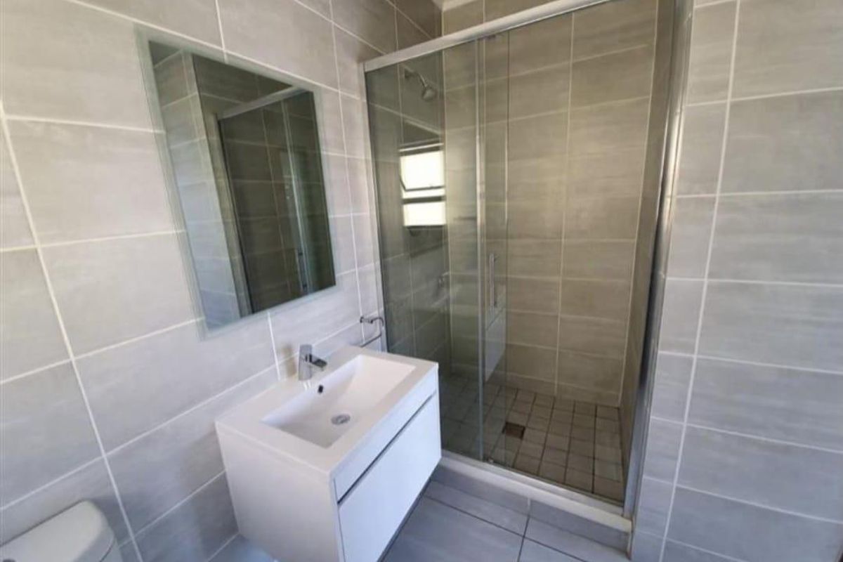 Modern bathroom featuring a wall-mounted vanity, a glass-enclosed shower, and neutral ceramic tiling throughout.
