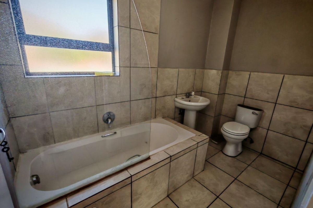 A functional bathroom featuring a built-in bathtub with a glass shower screen, a pedestal basin, and a standard toilet with tiled walls and flooring.