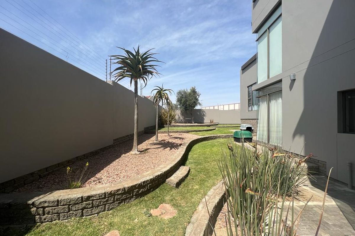 A well-maintained rear garden featuring tiered landscaping, stone retaining walls, manicured lawn, and established trees adjacent to the modern building exterior.