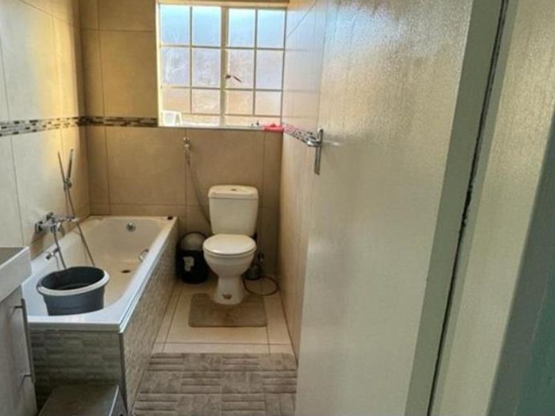 A functional bathroom featuring a bathtub, toilet, and vanity with neutral wall and floor tiling.